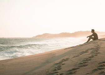 hombre sentado en la playa al atardecer
