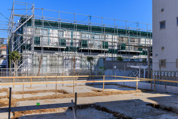 住宅建設予定地と外壁塗装のための足場に囲まれた2階建てアパート
