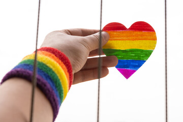 man with LGBT rainbow wrist band and lifting up a paper heart out of a wire fence