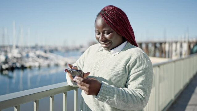 African woman with braided hair using smartphone at seaside