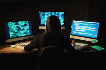 Unraveling the code. Rearview shot of a young hacker cracking a computer code in the dark.