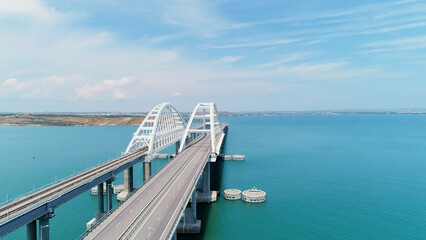Fototapeta na wymiar A long bridge for vehicles to cross the ocean. Drone view. Shot. A beautiful panorama overlooking the sunny clear sky and cars moving over a huge clear pond.