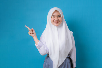Portrait of teenager Muslim female student in hijab pointing at copy space