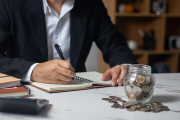 Man putting coins in piggy bank and taking notes in notebook money saving concept business