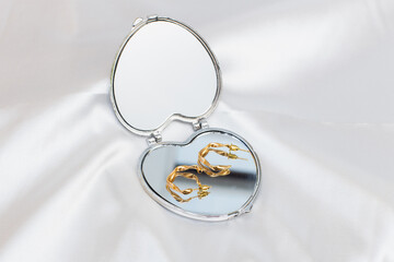 Elegant gold jewelry and mirror on white fabric, closeup