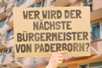 The question " Who's the next mayor of Paderborn? " on a banner in men's hands blurred the background. Election. City management. Politics. Urban. Voter. Candidate