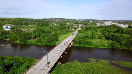 Aerial top down view of small road bridge across the river in rural area. Clip. Cars driving on the bridge and green vegetation.