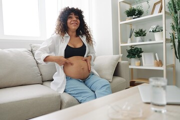 Pregnant woman smile and happiness sits on the couch freedom and strokes her belly feels kicks with the baby in the last month of pregnancy, mother's day lifestyle