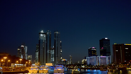 View from the river on the night city with skyscrapers and many lights. Action. Ships and yachts flowing along the river at night.