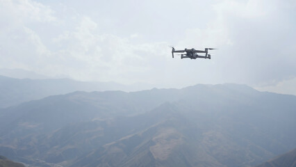 Fototapeta na wymiar Drone quad copter against mountain in morning haze. Action. Video shooting of forested hills.