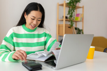 Young adult asian woman calculating home expenses and tax bills at home