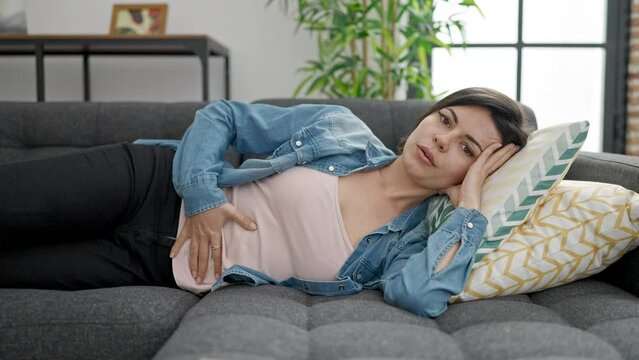 Young caucasian woman suffering for stomach ache lying on sofa at home