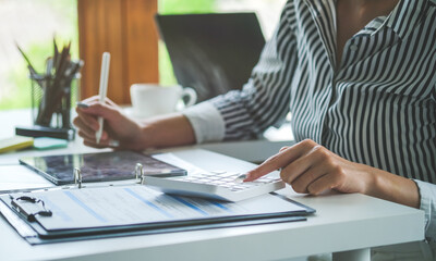 Cropped shot of businesswoman using calculator and writing information on notebook..
