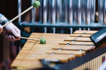 A musician with green mallets playing the marimba during a casual orchestra rehearsal
