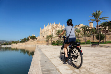 Adventure Travel Woman on a Bicycle riding near Catedral-Basilica de Santa Maria de Mallorca in Palma, Balearic Islands, Spain. Sunny Day. © edb3_16