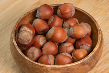Hazelnuts in shells in wooden bowl on wooden background close up. Whole and shelled organic...