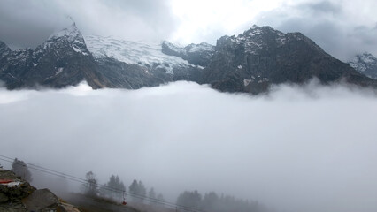 Fly over majestic mountain peaks and a fog. Creative. Valley covered by clouds and mountains on the background.