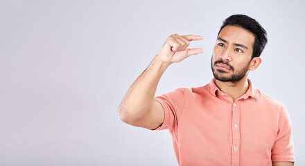 Hand gesture, size and mockup with a man in studio on a gray background to measure product placement space. Tiny, small and scale with a handsome young male sizing or measuring mock up on a wall