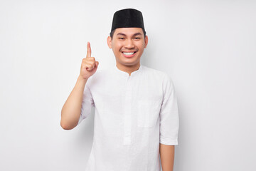 Cheerful Young Asian Muslim man in Arabic costume having creative idea, pointing his finger up at...