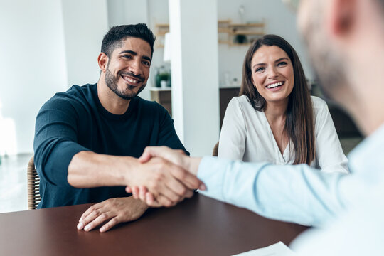 Attractive real-estate agent shaking hands with young couple after signing agreement contract in the office.