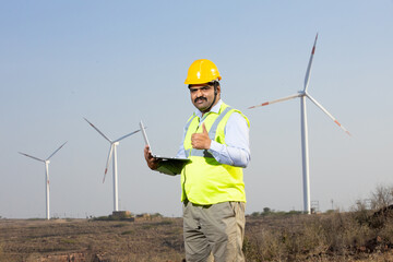  Renewable energy.- Indian engineer with laptop at windmill farm operation to generate electricity,...