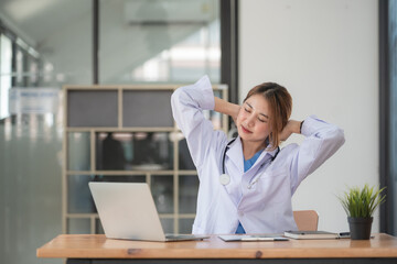 Shot of beautiful mature female doctor stretching body for relaxing while working with laptop in the consultation.