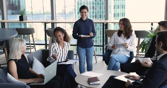 Multi ethnic colleagues listen to African businesswoman, team leader attending group meeting, morning briefing in modern skyscraper office. Share opinion, information, brainstorming, project planning