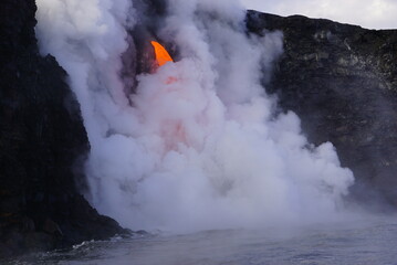 Hot lava stream flowing down from high cliff  into the ocean surrouded by white steam