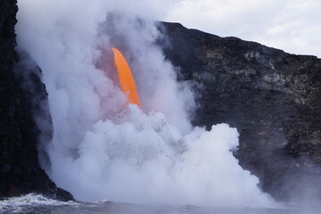 Fototapeta na wymiar Hot lava stream flowing down from high cliff into the ocean surrouded by white steam