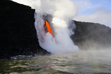 Hot stream of flowing lava surounded by white steam folling down from high cliff, Hawaii