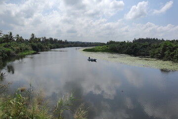 A river landscape view with a man on an Outrigger boat, the sky reflected on the river