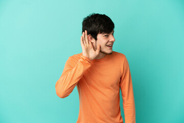 Young Russian man isolated on blue background listening to something by putting hand on the ear