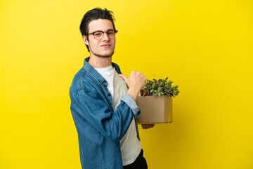 Russian Man making a move while picking up a box full of things isolated on yellow background proud...