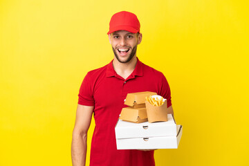 pizza delivery man picking up pizza boxes and burgers over isolated background with surprise facial...