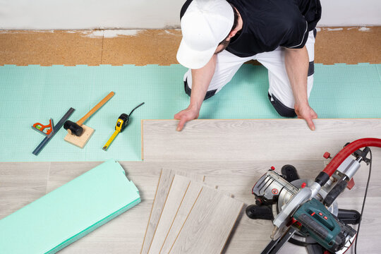 male worker laying laminate oor vinyl flooring. tools like chop saw hammer rolling measure gray laminate tiles on footstep sound insulation. diy professional home improvement and renovation concept.