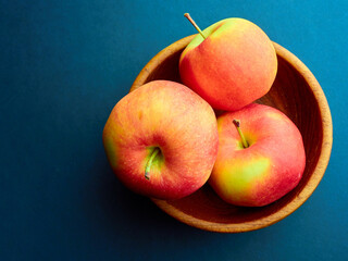 Ripe yellow-red apples in a wooden bowl on a blue background.