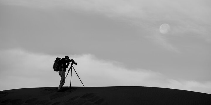 A photographer shooting on a ridge in with the moon above.