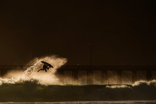 Surfer takes flight off a wave into final light of the day