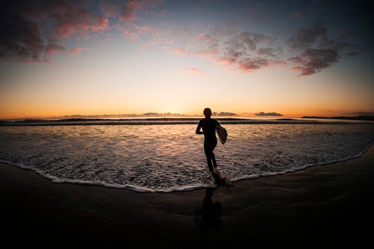 Surfer walks towards the waves at sunset
