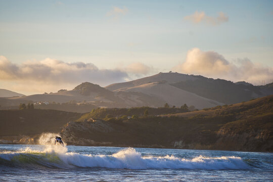 Surfer boosts air in front of mountain coastline