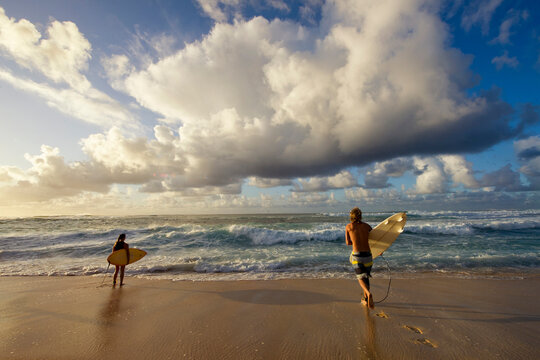Two surfers run out to surf under the sunset