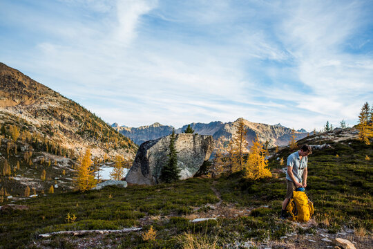 A backpacker unpacks alongside the colorful larch trees and steep mountains of the Cascades in the Pasayten Wilderness on the Pacific Crest Trail (PCT) in Washington.