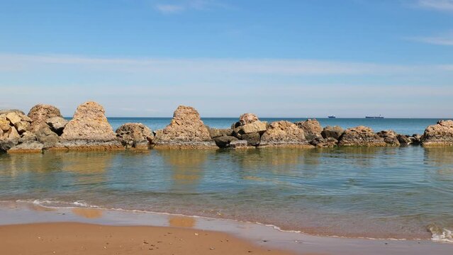 Waves during the day on the sea with stones. Blue Sky