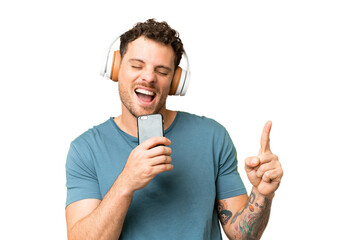 Brazilian man over isolated chroma key background listening music with a mobile and singing