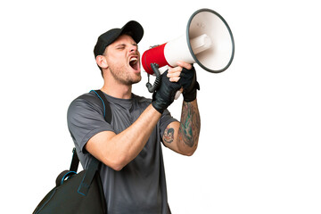 Young sport man with sport bag over isolated chroma key background shouting through a megaphone