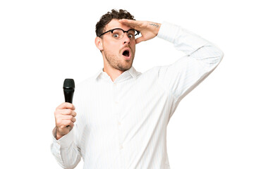 Brazilian man picking up a microphone over isolated chroma key background doing surprise gesture...