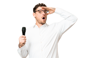 Brazilian man picking up a microphone over isolated chroma key background doing surprise gesture while looking to the side