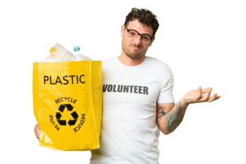 Brazilian man holding a bag full of plastic bottles to recycle over isolated chroma key background making doubts gesture while lifting the shoulders
