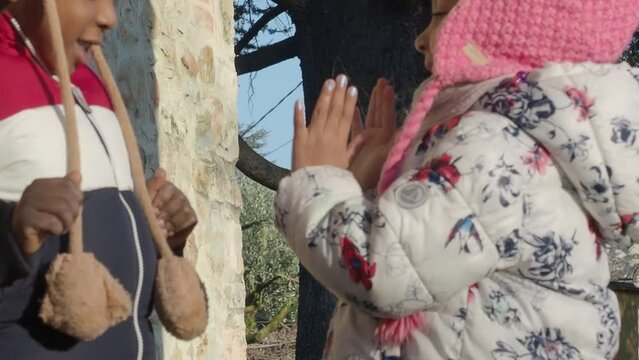 happy african american little kids playing outdoors a sunny day in cold weather wearing winter fashion and beanie knit hats with earflaps