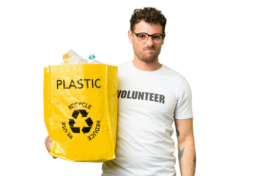Brazilian man holding a bag full of plastic bottles to recycle over isolated chroma key background with sad expression
